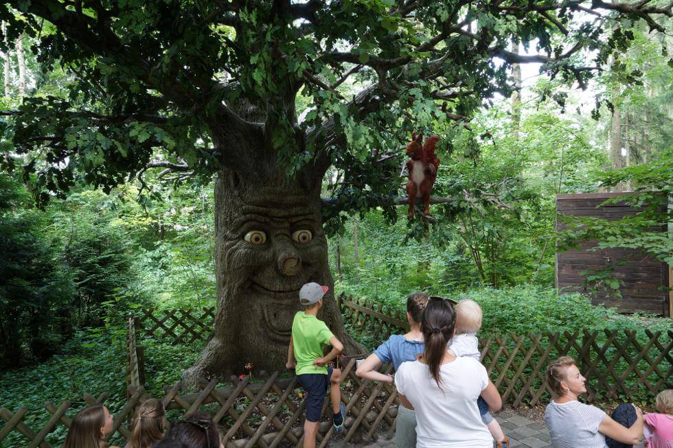 Kinder vor einem Baum mit Gesicht und Eichhörnchen auf dem Ast