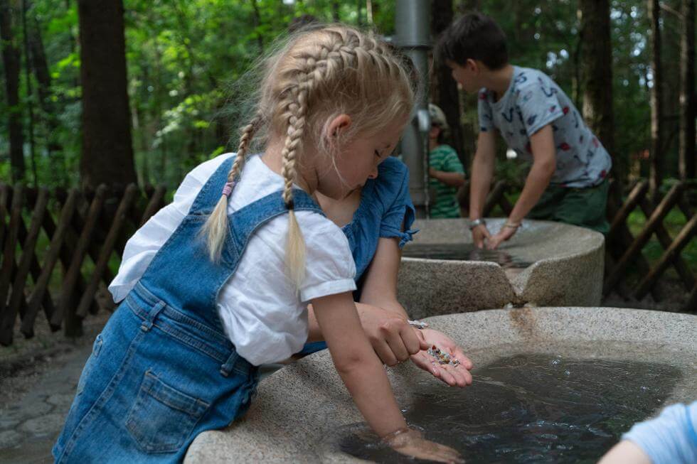 Kleines Mädchen sucht Edelsteine aus einem Wasserbecken im Freizeitpark Märchenwald Isartal