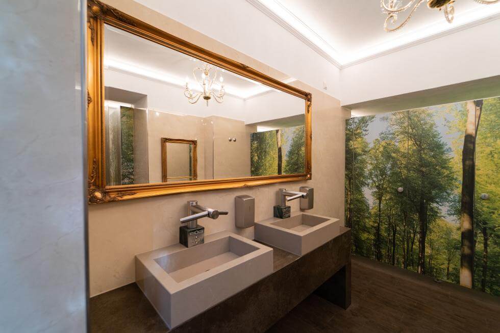 Waschbecken mit großem Spiegel bei den Toiletten und Wald-Tapete